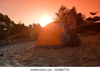 Malang, Indonesia - May 7 2022: silhouette of a tent and a mother on the beach at sunrise on the coast of Goa Cina, Malang City, Indonesia