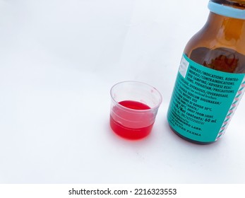 Malang, Indonesia - October 20 2022 : Red Syrup For Children Medicine In Measuring Cup And Prescription Bottles With Indications, Composition And Warning Labels.