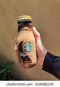 Malay Lady Hand Holds A Glass Bottle Of Starbucks Frappucino Ready To Drink Coffee. Famous Brand. Sunkissed. Brown Wall Background. Chill And Shake Well. Mocha Flavor Beverage. Malaysia. April 2022