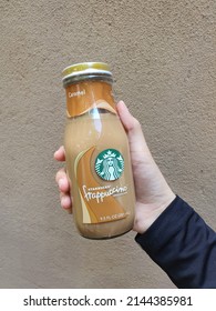 Malay Lady Hand Holds Starbucks Frappucino Chilled Coffee Drink. Halal Ready To Drink Coffee With Caramel Flavor. Glass Bottle. Brown Wall Background. Malaysia. April 2022