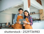 Malay man and woman wearing apron smiling on a tablet together in a coffee shop