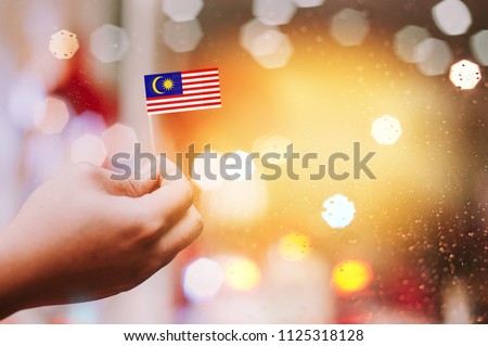 Malaysia Independence Day celebration.Man's hand holding small Malaysian flag with bokeh background.