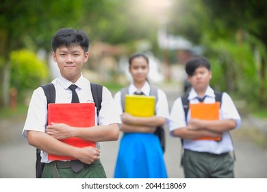 Malaysian Students Holding A Book While Carrying Their Bagpack.Secondary School Teenagers In The Outdoor Portrait.Chinese And Kadazan Dusun Ethnic Wearing School Uniform In Malaysia. Education In Asia