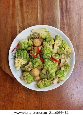 Malaysian style stir fried Romanesco broccoli or Roman Romanesque cauliflower. Cooked with oyster sauce, red chili and fish cake. White plate with wooden  tray . Green flower bud. High nutrition.