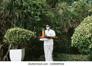 Maldives - August 2021: Maldivian Waiter, Hotel Worker In Protective Face Mask, Carries Serving Tray Of Drinks And Snacks To Swimming Pool On Luxury Tropical Island Resort