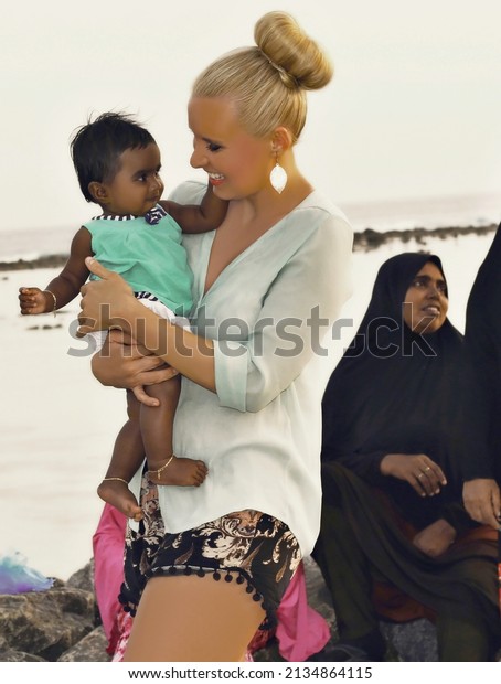 MALDIVES –\
THULUSDHOO – JANUARY 2020 - Czech traveller Lenka Kopalova posing\
with cute baby girl with a large Maldivian family watching the\
sunset on the island in the\
background.