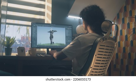 Male 3D designer sitting at the table at home and making animation for video game character, using modern computer and software for creating 3D modeling projects