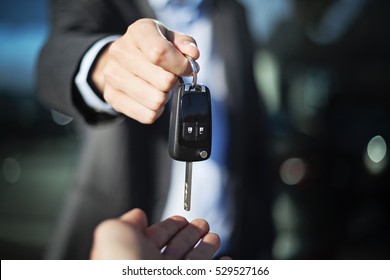 Male Adult Dealer Hand Giving Car Keys To Female Person, Close-up Photo Outdoor, Sunny Day, Caucasian Man In Suit