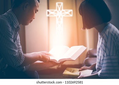 Male adults are reading the Holy bible by pointing to the character and to share the gospel to youth. The cross symbol, glow over the books of the Bible, Concepts of Christianity.