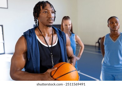 Male african american basketball coach holding ball, instructing female players during practice. coaching, training, teamwork, sports, exercise, guidance - Powered by Shutterstock