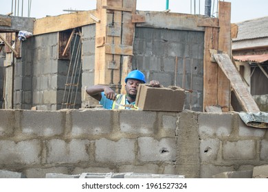 A MALE African Construction Worker Using A Trowel To Build A Fence On A Building Site And He Is Wearing A Blue Protective Helmet And A Green Reflective Traffic Jacket To Earn A Living 