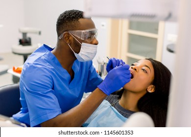 Male african dentist examining a patient with tools in dental clinic. African female patient getting dental treatment in dental clinic - Shutterstock ID 1145601353