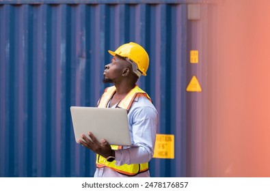 Male African engineer worker wearing yellow hard hat and reflective safety vest using laptop computer for container inspection at cargo shipyard. Transportation logistic industry concept. - Powered by Shutterstock