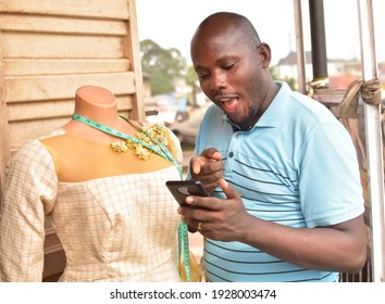 A Male African Nigerian Fashion Designer With A Phone Measuring Tape And A Mannequin  