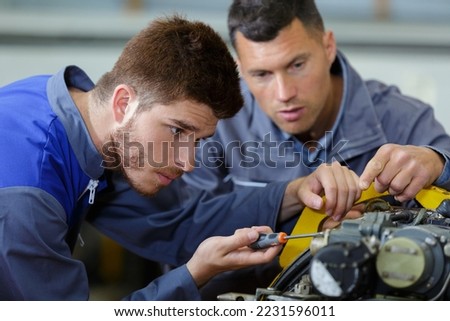 male apprentice engineer using screwdriver under supervisors guidance