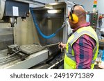 Male apprentice engineer working with CNC machine in factory	
