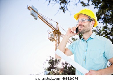 Male architect with blueprint talking on mobile phone against view of a crane