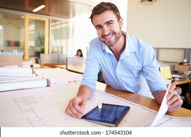 Male Architect With Digital Tablet Studying Plans In Office