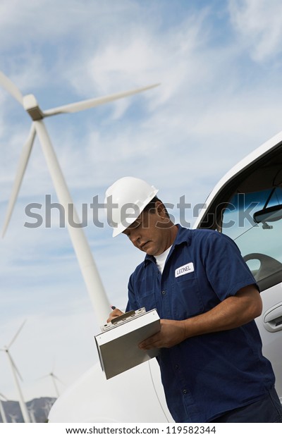 Male architect noting down on clipboard at wind\
mill farms