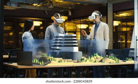 Male architect uses VR headset and wireless controllers, presents modern hi-tech building and park architectural project in virtual reality to colleagues. 3D hologram. Future digital AI technologies. - Powered by Shutterstock