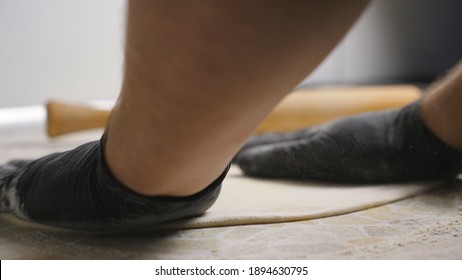 Male Arms Of Cook In Gloves Forming Pastry On A Wooden Surface At Cuisine. Hands Of Chef Shaping Floured Dough For Pizza On A Kitchen Table At Restaurant. Concept Of Preparing Food. Close Up Slow Mo