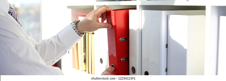 Male Arms Pick Red File Folder From Office Book Shelf Closeup. Store Pile Of Project Documentation Concept