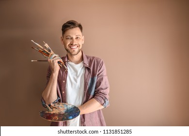 Male artist with paint tools and palette on color background