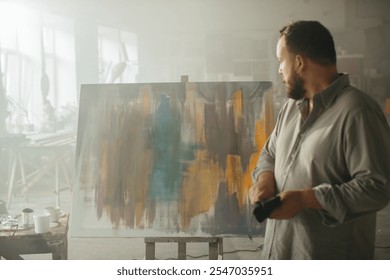 Male artist thoughtfully looking at a freshly completed painting in his studio. - Powered by Shutterstock