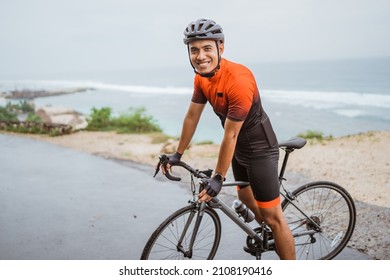male asian cyclist with red and black jersey standing on his bike - Shutterstock ID 2108190416
