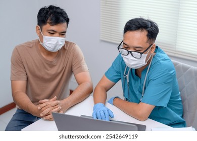 A male Asian doctor wearing a mask uses a laptop computer during an outbreak to discuss treatment plans - Powered by Shutterstock