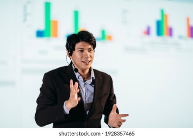 Male Asian Speaker Stands On Stage For Business Presentation 