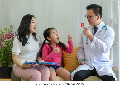 Male Asian Speech Therapist Showing R Letter To Asian Girl During Visit With Mother In Clinic. Concept Of Cure For Kid With Speaking Problem.