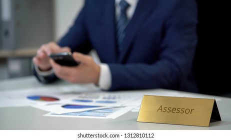 Male assessor in business suit using smartphone, working on important documents