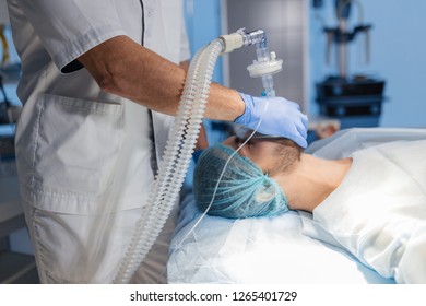 Male assistants prepares a patient to invasive surgery in the Hospital operating room, holding oxygen mask over man s face, close up - Shutterstock ID 1265401729