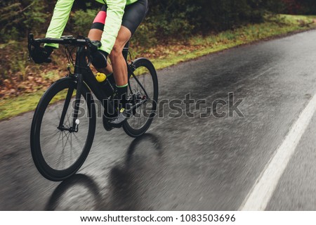 Male athlete in cycling gear riding bike on wet road. Low section shot of cyclist training outdoors on a rainy day.