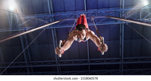 Male athlete doing a complicated exciting trick on gymnastics rings in a professional gym. Man perform stunt in bright sports clothes - Powered by Shutterstock