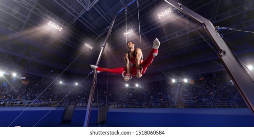 Male Athlete Doing A Complicated Exciting Trick On Gymnastics Rings In A Professional Gym. Man Perform Stunt In Bright Sports Clothes