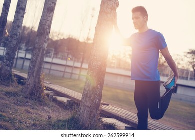 Male athlete doing stretching muscles for running in the park at sunset (intentional sun glare and vintage color)