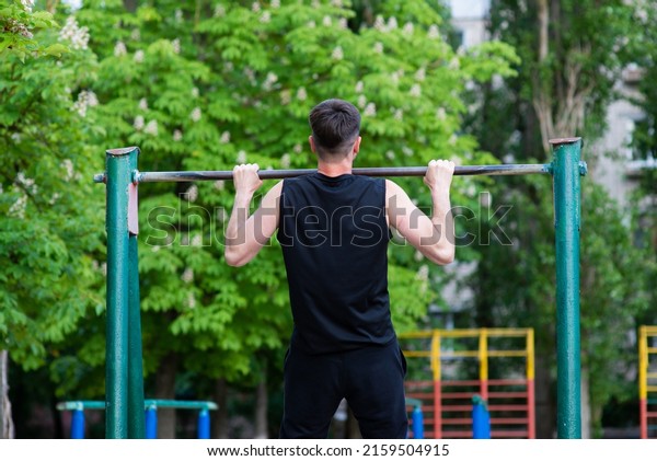 A male athlete is engaged in a horizontal bar, view\
from the back
