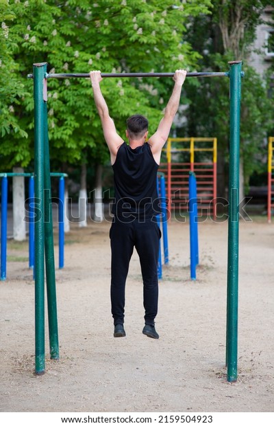 A male athlete is engaged in a horizontal bar, on\
a sports ground