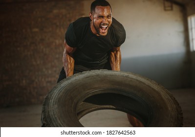 Male athlete flipping heavy tire inside an abandoned warehouse. Strong man flipping a tyre during an intense training session in a cross workout space. - Powered by Shutterstock