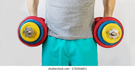 Male Athlete Holding Up Heavy Dumbbells In Two Hands. Home Workouts During The Coronavirus Pandemic: A Healthy Lifestyle Concept.Banner