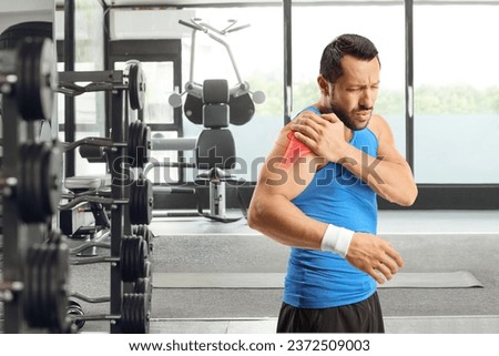 Male athlete holding inflamed shoulder at the gym