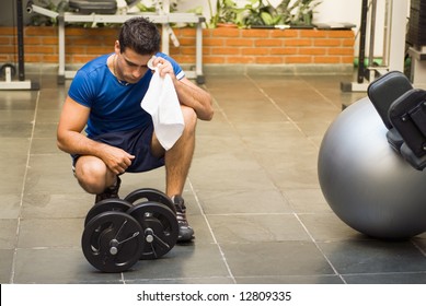 Male Athlete Kneeling Down By Dumbbells Toweling Sweat Of His Brow.