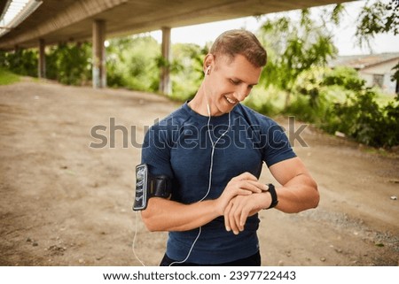 Male athlete looking at his smart watch or tracker under bridge