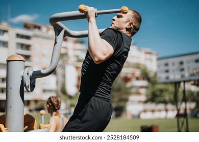 Male athlete performing pull-ups on outdoor fitness equipment in a city park. Healthy lifestyle and strength training. Summer day workout. - Powered by Shutterstock