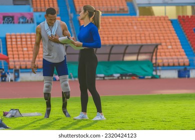 Male athlete with prosthetic blades, alongside female trainer, outlining the day's speed running training at the sports stadium - Powered by Shutterstock