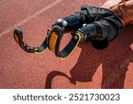 Male athlete with prosthetic legs on a brick colored running track. Prosthetic legs in action. Athletic prosthetic legs for running. Male athlete showcasing prosthetic legs. Photo of a sport man.