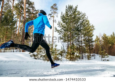 male athlete runner running through forest winter trail
