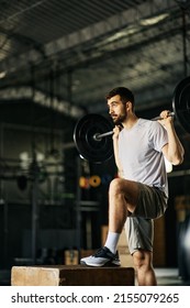 Male athlete stepping up on crate while exercising with barbell during sports training in a gym.